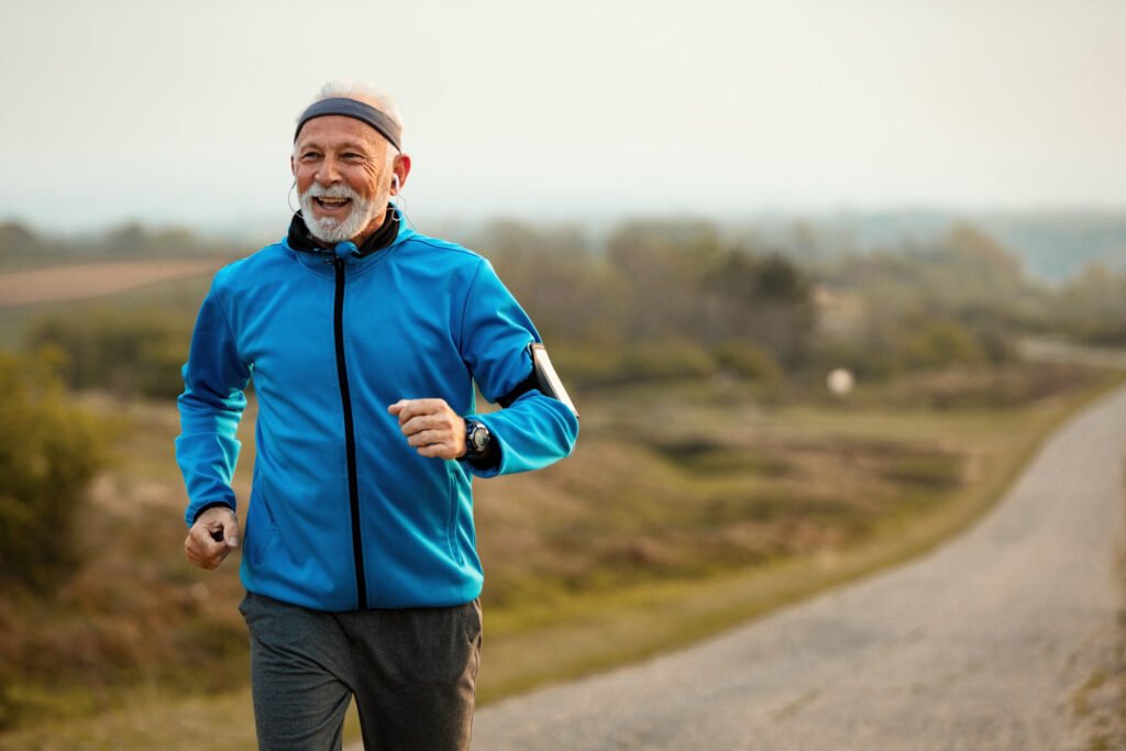 happy mature athletic man running in nature while listening music on earphones.